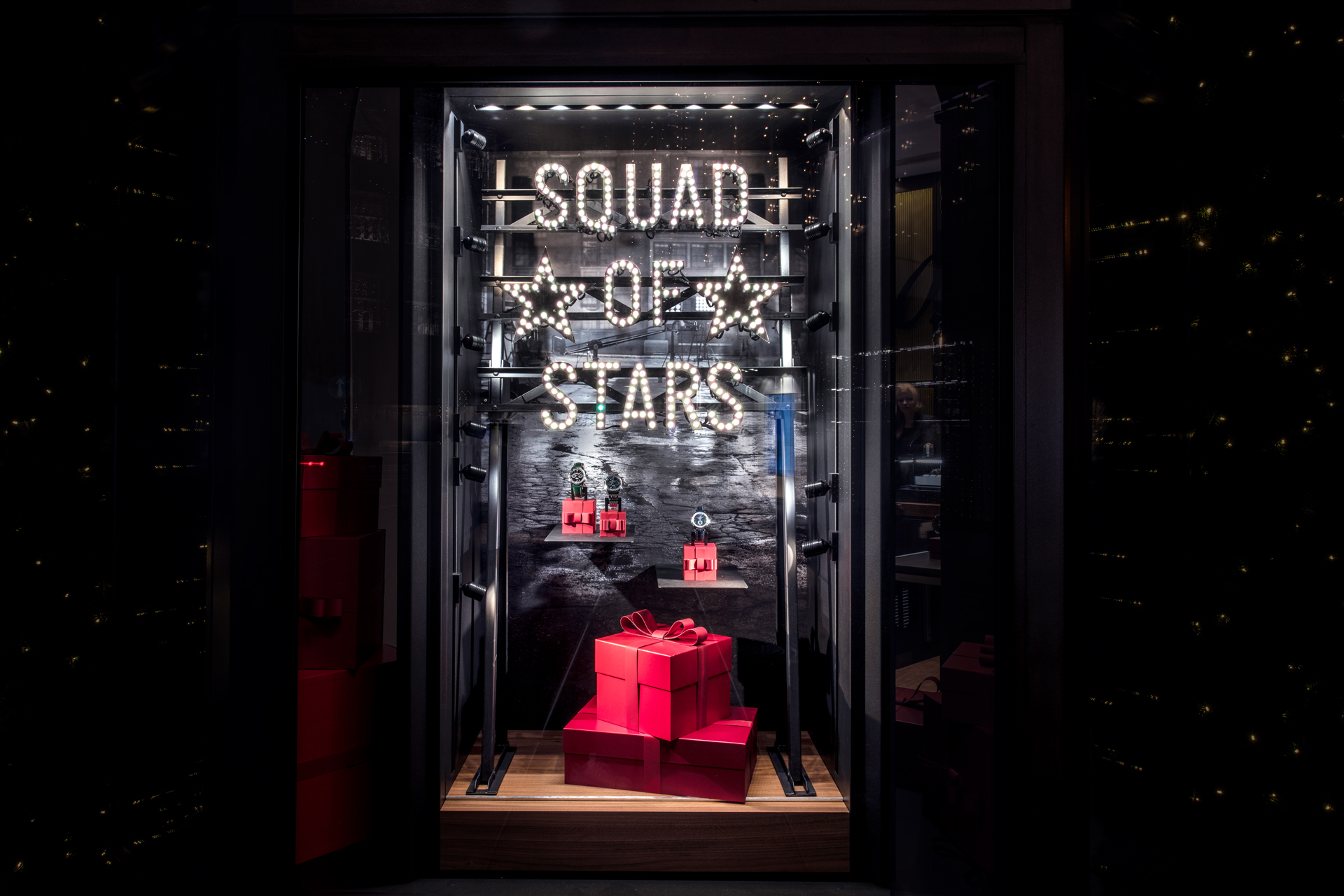 Breitling-Schaufenster mit "Squad of Stars"-Leuchtschrift und roten Geschenkschachteln, gestaltet von MORE PIOUS STUDIOS.