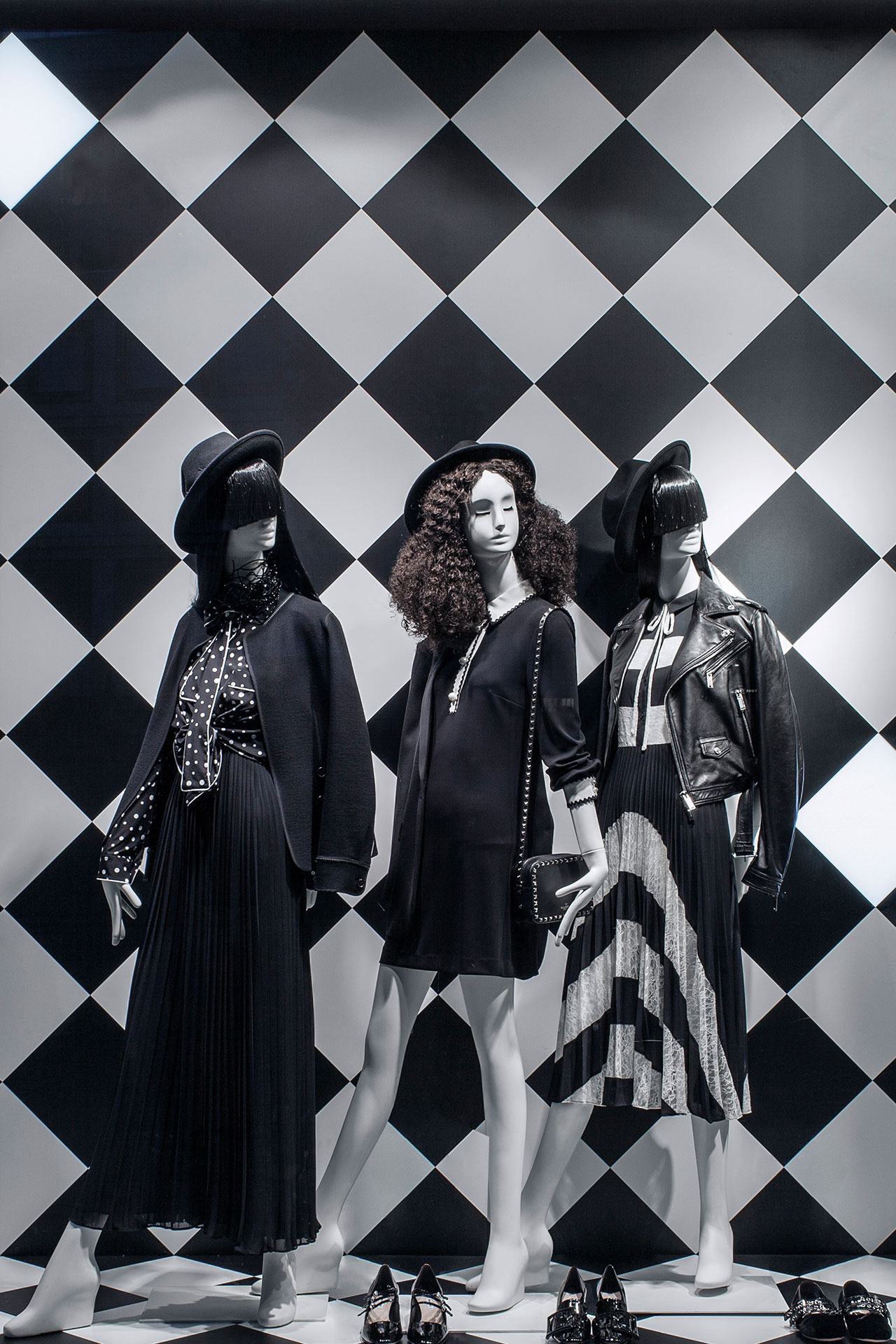 Schaufensterdisplay bei Breuninger mit drei Mannequins in Schwarz-Weiß-Mode vor einem kontrastreichen Rautenmuster-Hintergrund, gestaltet von MORE PIOUS STUDIOS für Visual Marketing und window system.