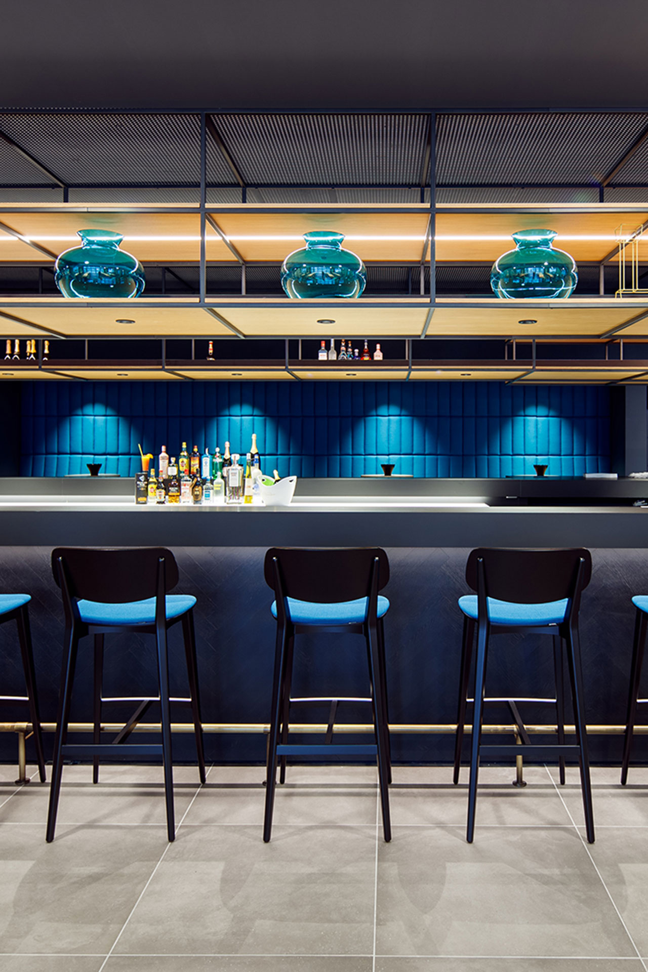 Design-Bar mit moderner Beleuchtung und blauen Akzenten im ArtHotel Ana in Göppingen, entworfen von MORE PIOUS STUDIOS.