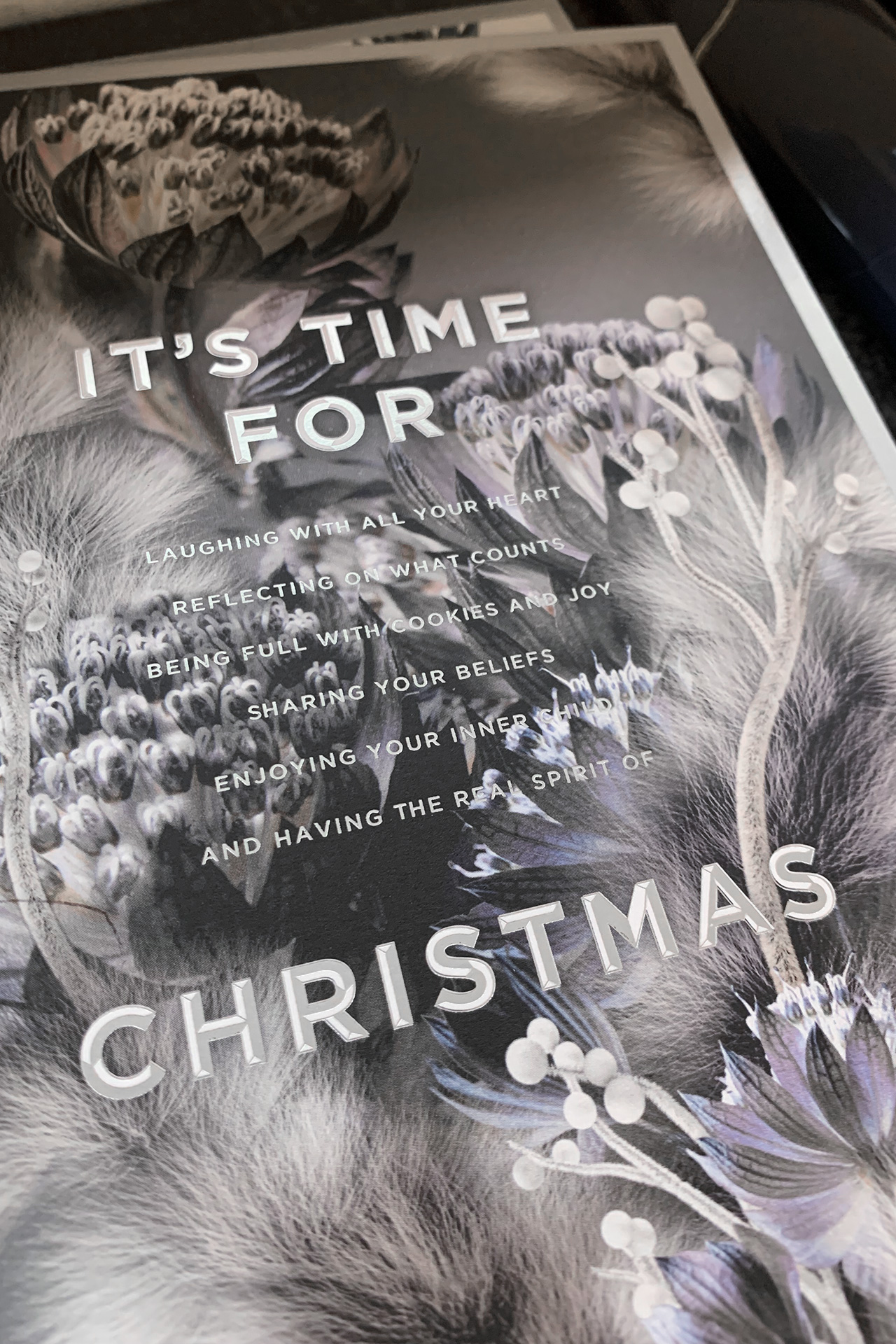 Nahaufnahme einer festlichen Weihnachtskarte von MORE PIOUS STUDIOS mit floralen Elementen und typografischen Details.