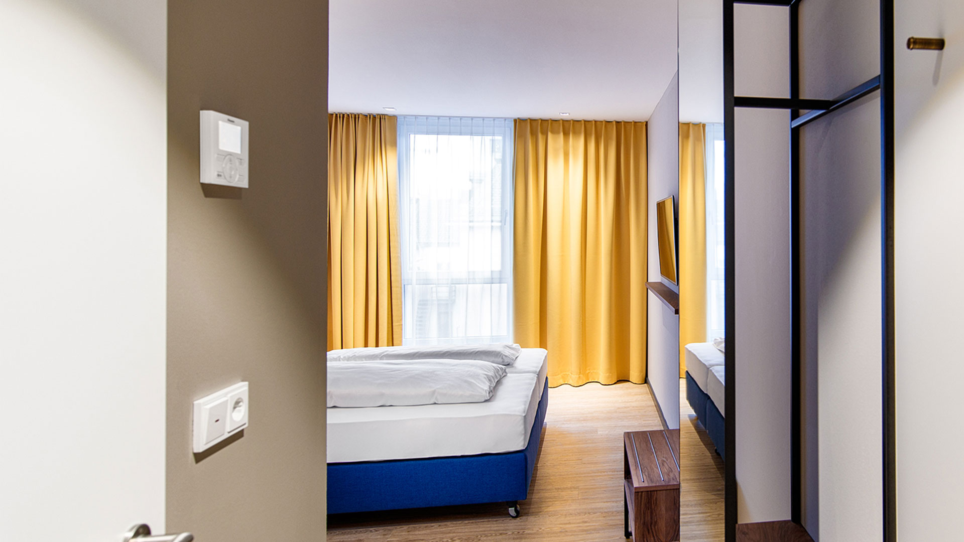 Hotelzimmer mit blauer Matratze und gelben Vorhängen im ArtHotel Ana, entworfen von MORE PIOUS STUDIOS.