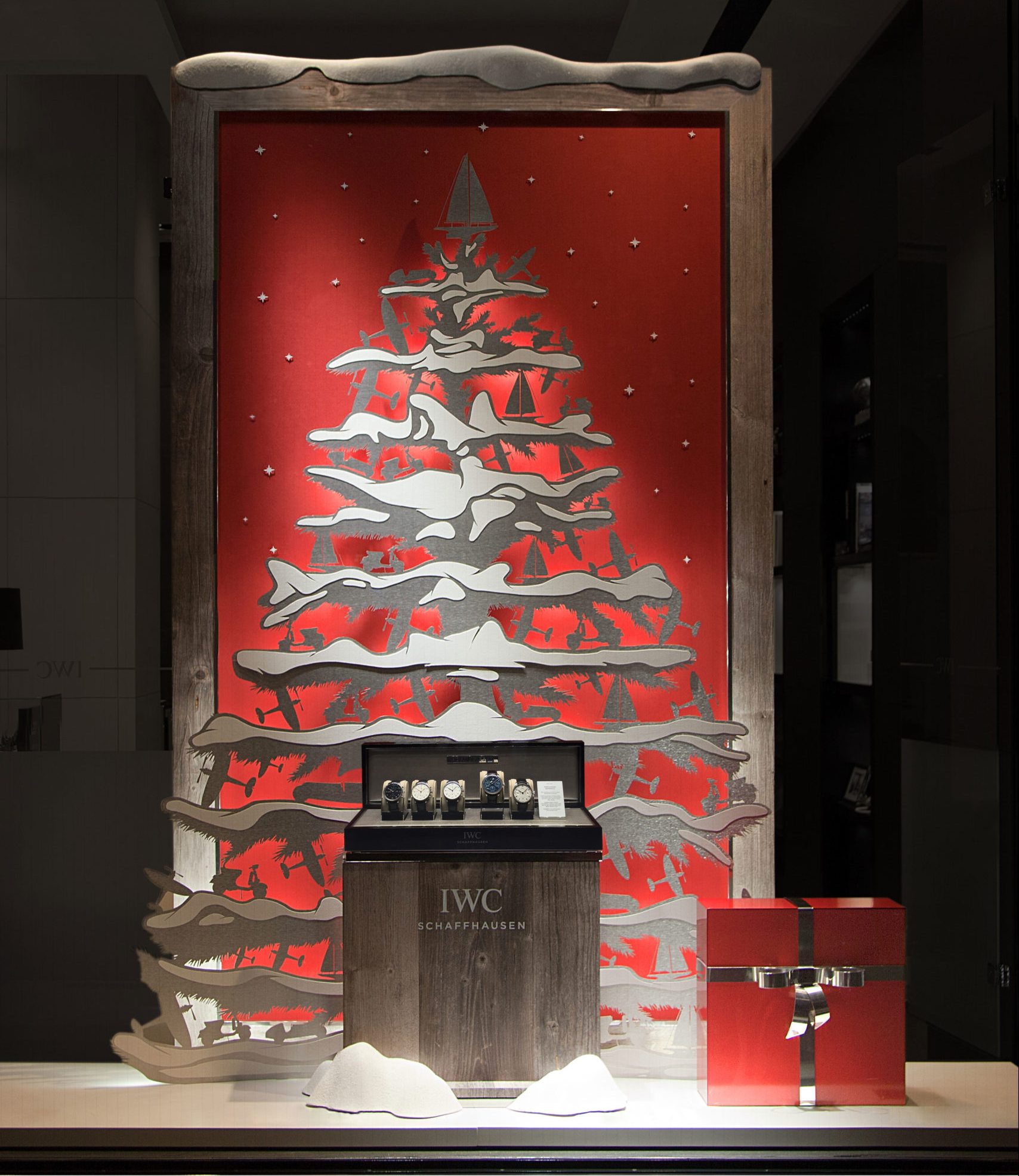 IWC-Weihnachtsfenster mit Scherenschnitt-Baum und rotem Hintergrund, gestaltet von MORE PIOUS STUDIOS.