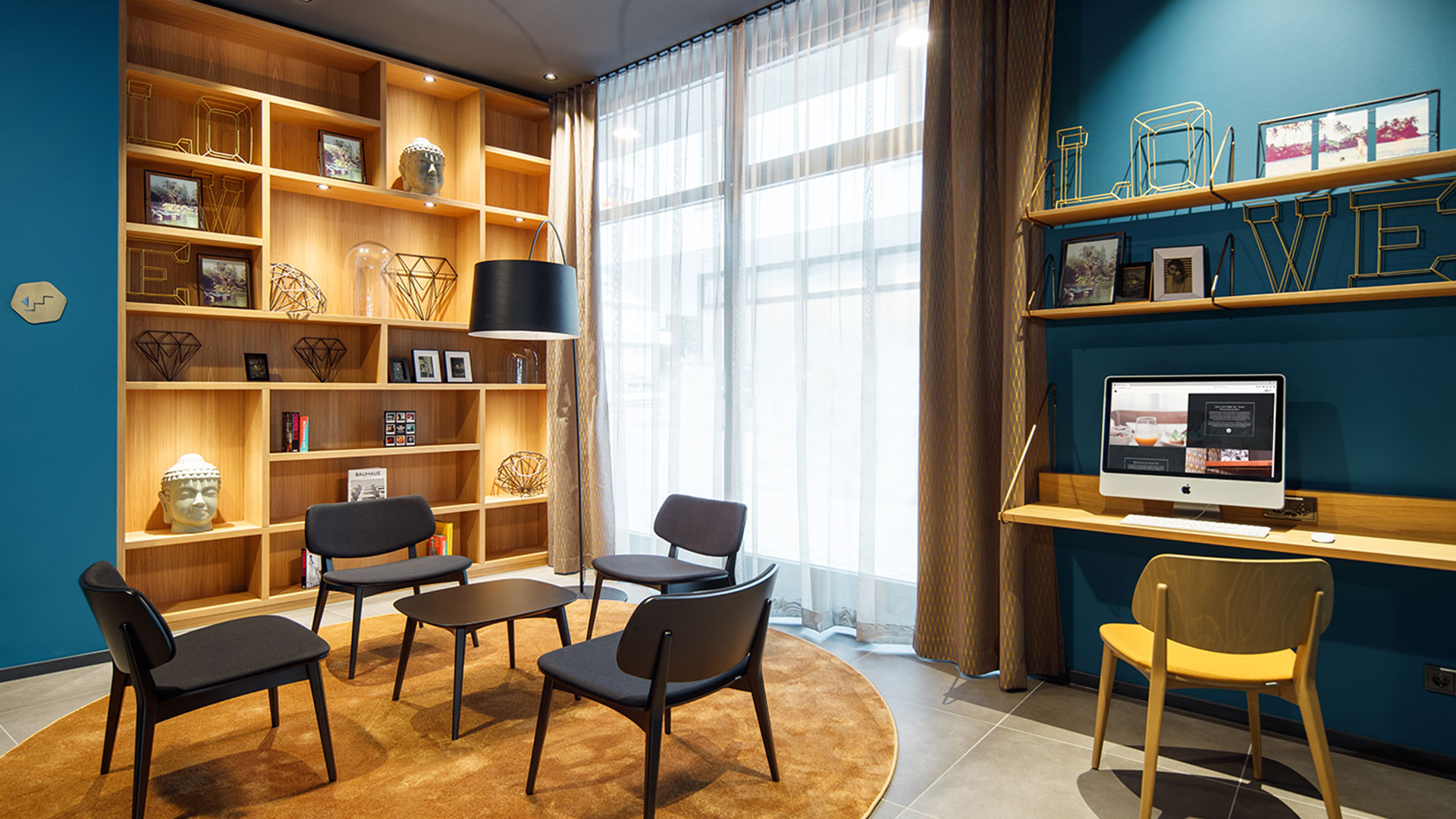 Lounge-Bereich mit Holzbibliothek, gemütlichen Sesseln und moderner Einrichtung im ArtHotel Ana, gestaltet von MORE PIOUS STUDIOS.