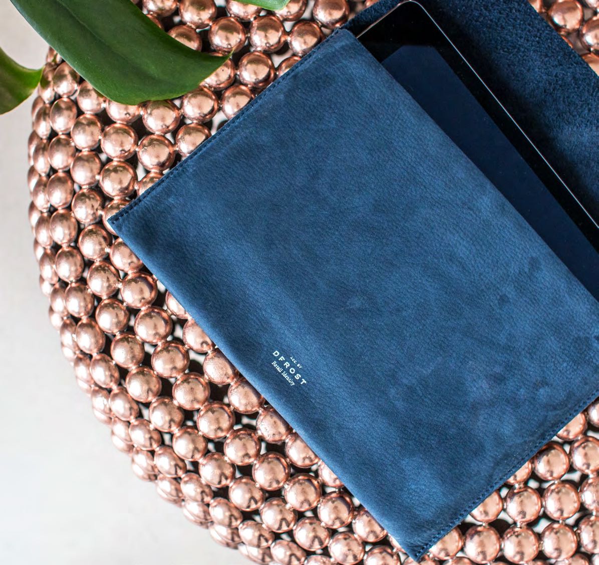 Navy-blaues Leder-Tablet-Etui von AYASSE, arrangiert auf einem kupferfarbenen Untergrund, kuratiert von MORE PIOUS STUDIOS im Projekt DFROST x AYASSE.