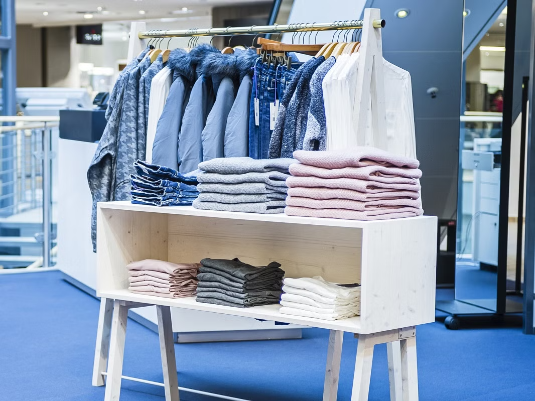 Minimalistisches Kleiderdisplay mit gefalteten Pullovern und hängenden Jacken, gestaltet von MORE PIOUS STUDIOS für den Pop-up-Store Homecoming.