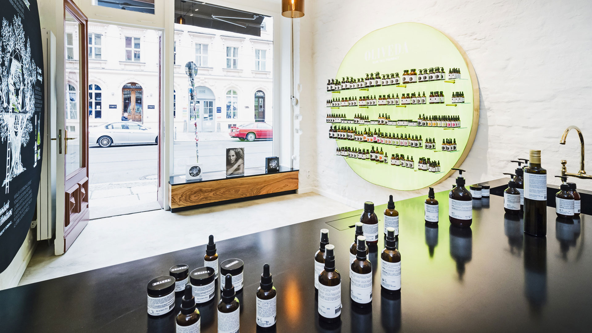 Oliveda Flagship-Store mit grün beleuchteter Produktwand und Schaufenster zur Straße