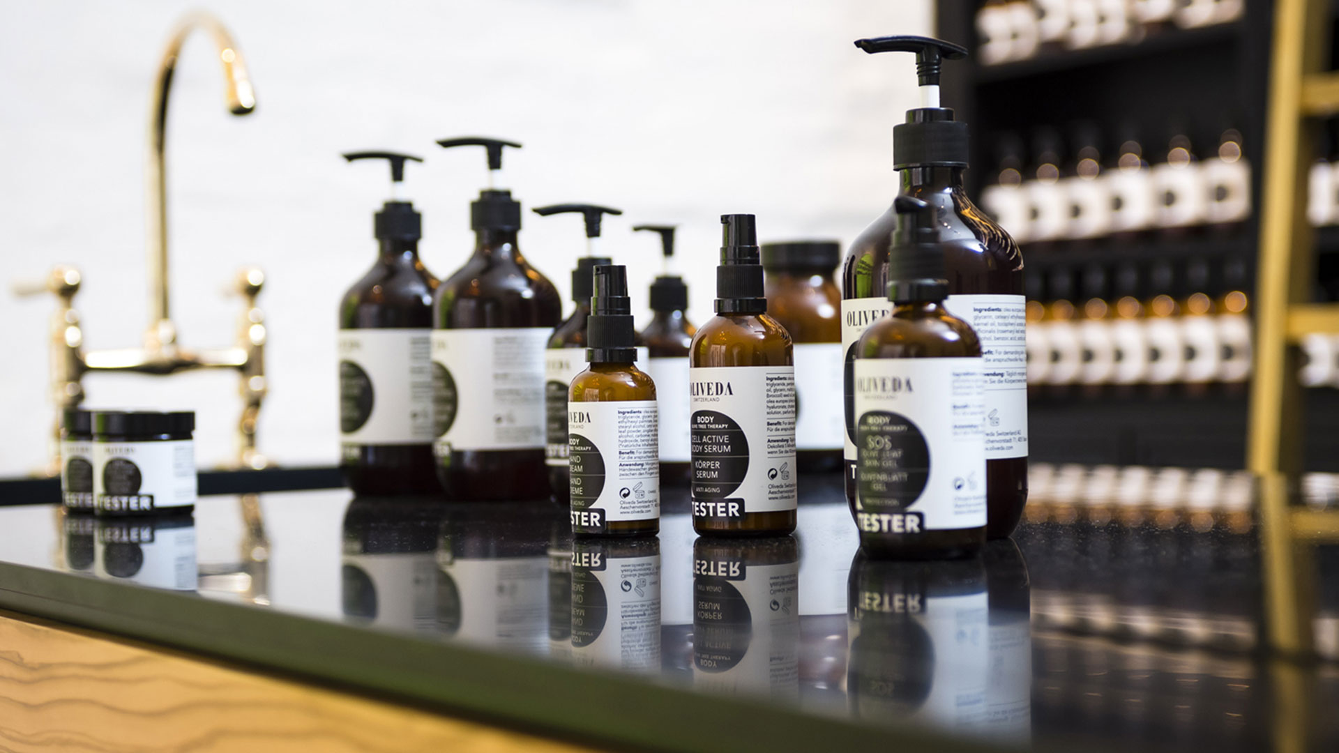 Nahaufnahme von Oliveda Pflegeprodukten auf schwarzer Theke mit goldenem Wasserhahn