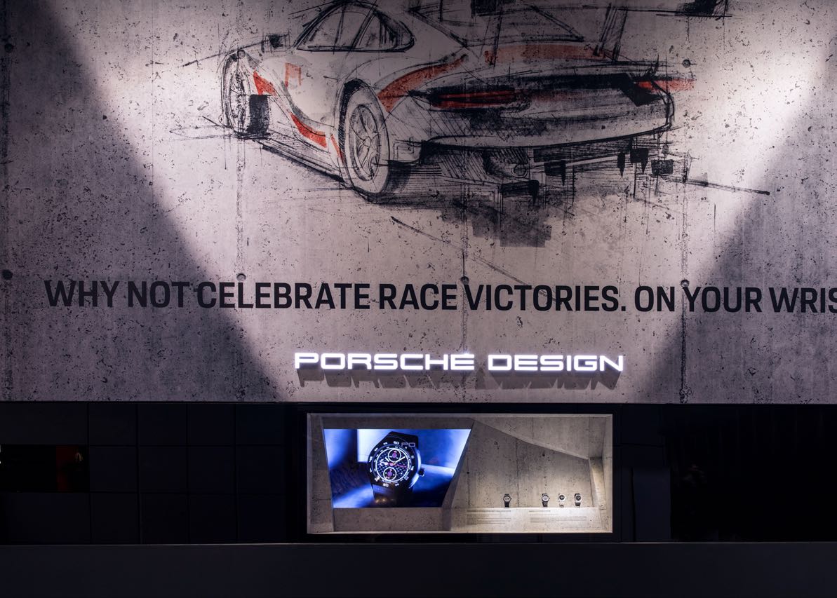 Detailansicht des Porsche Design Messestands mit einer Skizze eines Rennwagens und einer beleuchteten Vitrine für Uhren, gestaltet von MORE PIOUS STUDIOS.