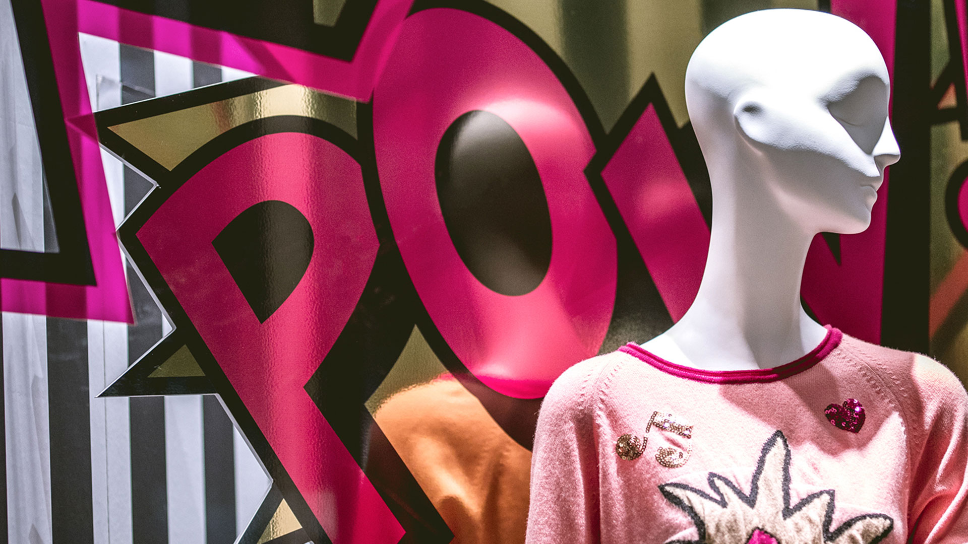 Nahaufnahme von Schaufensterpuppe mit pinkem Pullover und „POW!“ Hintergrund