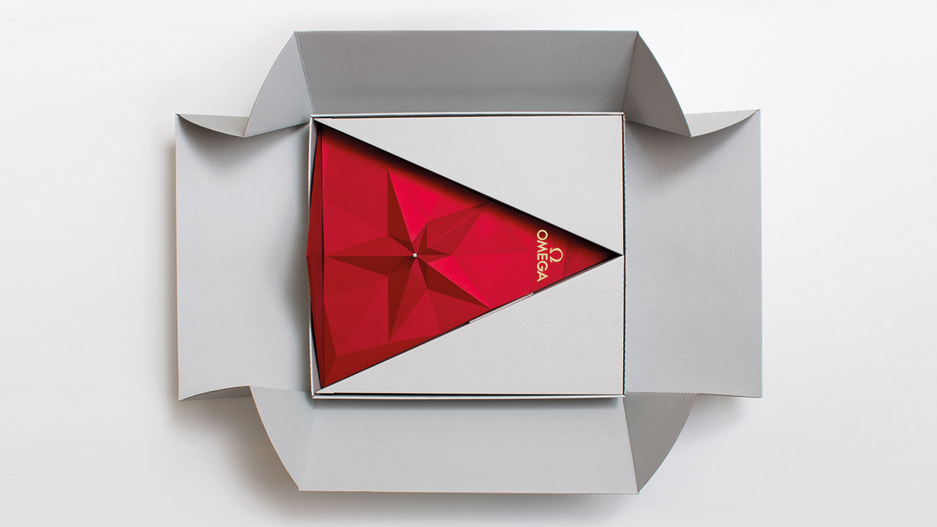 Geöffnete Verpackungsbox mit roter, dreieckiger Schachtel mit goldener Sternprägung von Omega.
