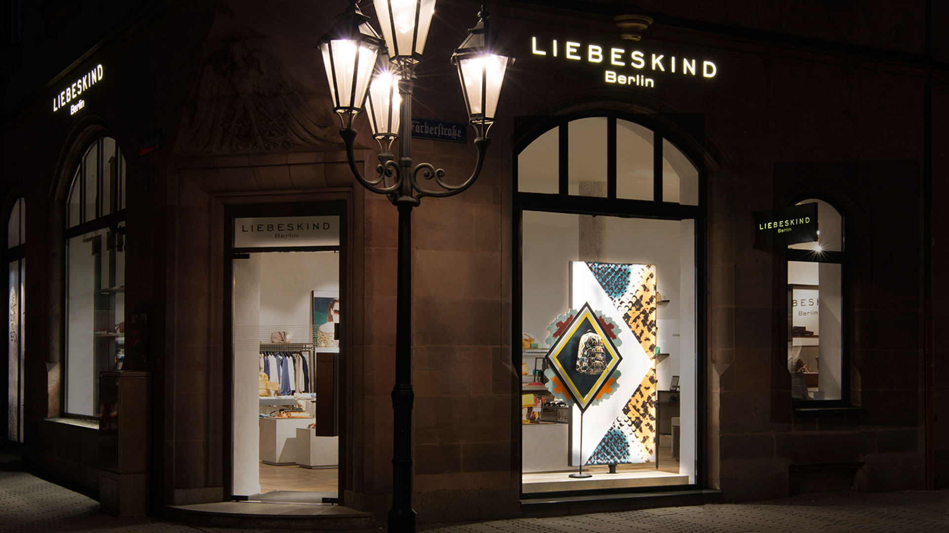 Nachtansicht des Liebeskind Berlin Stores mit beleuchtetem Patternity Summer Campaign Schaufenster, entworfen von MORE PIOUS STUDIOS.