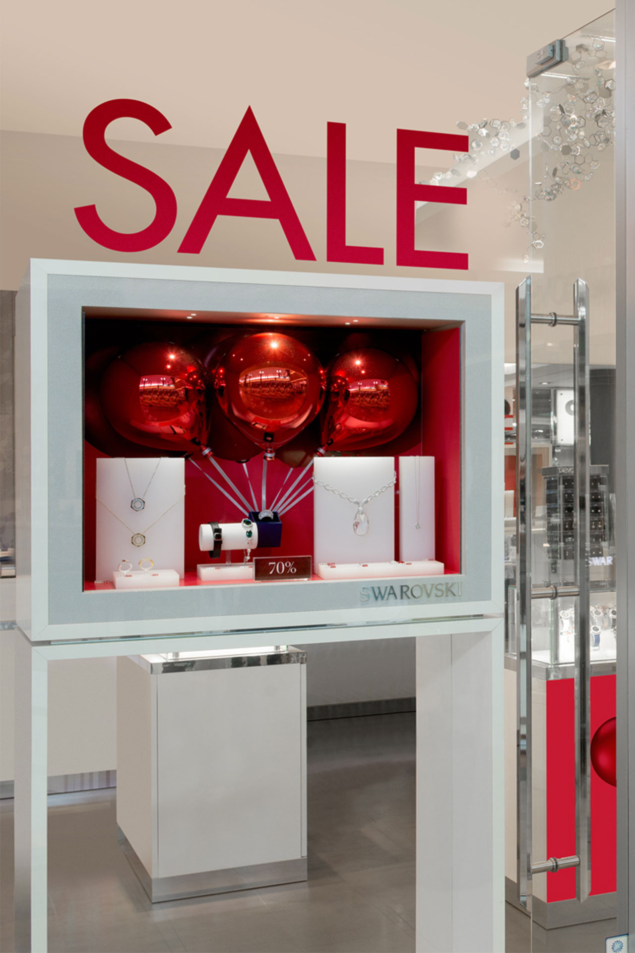 Schmuckdisplay mit roten Ballons und Sale-Schildern, das Swarovski-Schmuckstücke in einem Schaufenster hervorhebt.