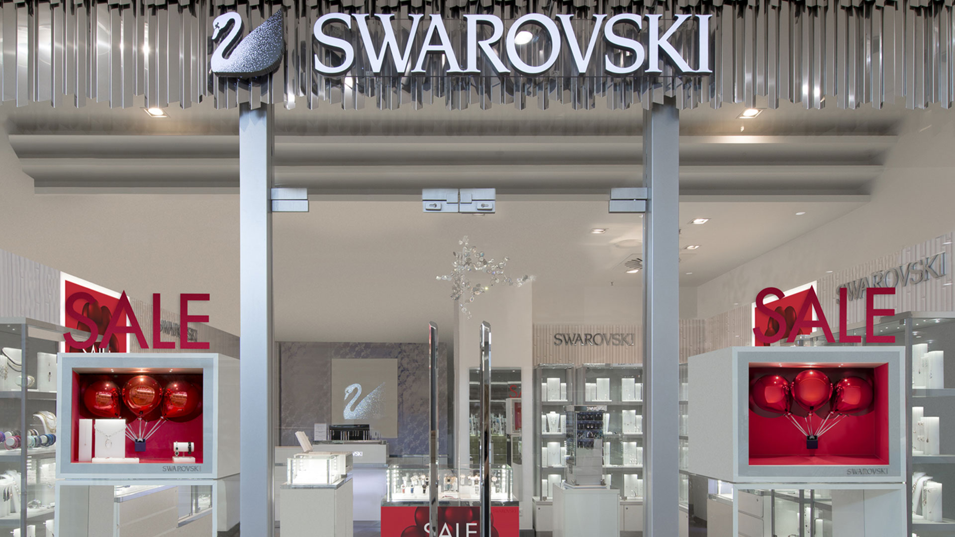 Swarovski-Storefront mit roten Sale-Schildern und dekorativen roten Ballondisplays.